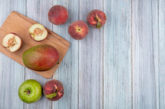 Vista superior de la mitad de duraznos en una tabla de cocina de madera con manzana de mango sobre una superficie de madera gris