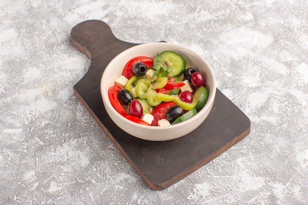 Vista superior de la mitad de la ensalada de verduras frescas con rodajas de pepinos, tomates, aceitunas y queso blanco dentro de la placa en el escritorio gris ensalada de comida vegetal color