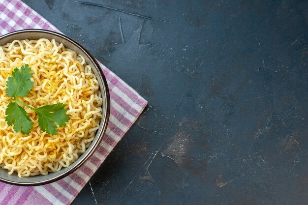 Vista superior de la mitad de fideos ramen asiáticos en un tazón sobre una toalla de cocina a cuadros blanca rosa sobre una mesa oscura con lugar para copiar