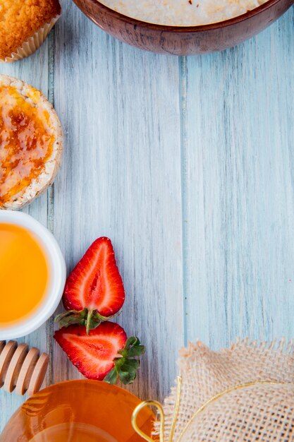 Vista superior de la mitad de fresas cortadas con avena crujiente jarabe de melocotón mantequilla de magdalena en la superficie de madera con espacio de copia