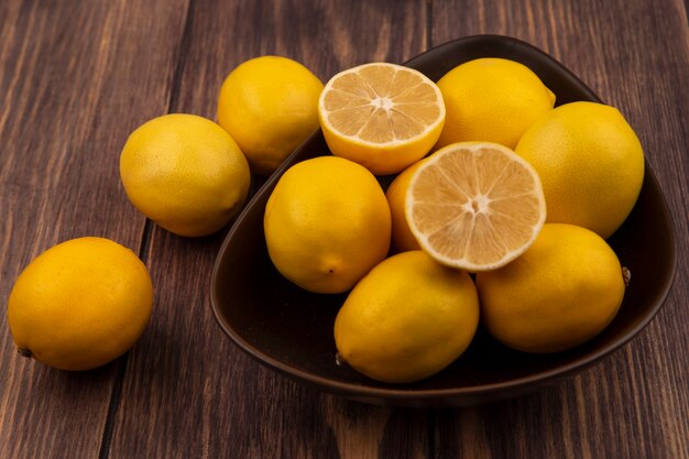 Vista superior de la mitad fresca y limones enteros en un recipiente con limones aislado sobre una superficie de madera