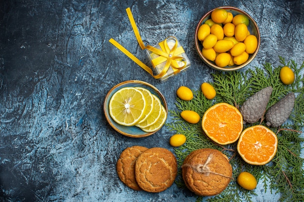 Vista superior de la mitad y frutas cítricas frescas enteras y caja de regalo amarilla conos de coníferas galletas apiladas sobre fondo oscuro