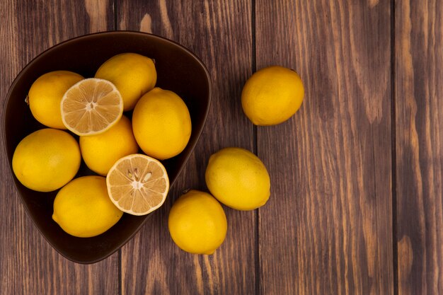 Vista superior de la mitad y los limones enteros en un recipiente con limones aislado sobre una superficie de madera con espacio de copia