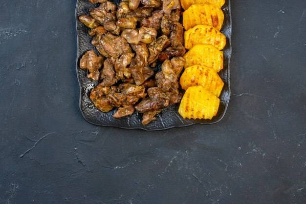 Vista superior de la mitad de las papas fritas de hígado de pollo con patatas en un plato negro sobre la mesa