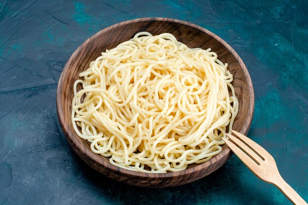 Vista superior de la mitad de la pasta italiana cocida dentro de la placa de madera redonda sobre la superficie azul pasta italia comida cena masa carne