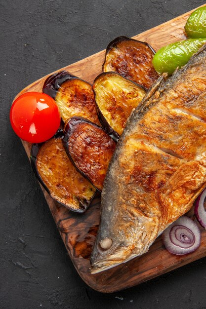 Vista superior de la mitad de pescado frito berenjenas fritas cebolla en tablero de madera sobre superficie oscura