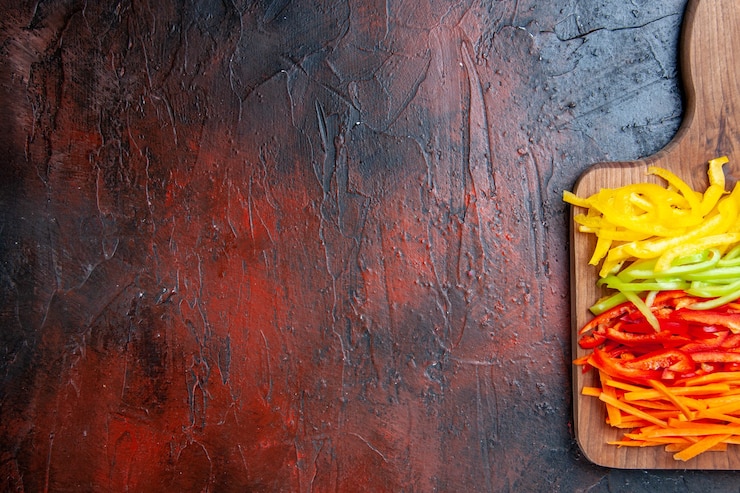 Foto gratuito vista superior de la mitad de los pimientos cortados de colores en la tabla de cortar en la mesa de color rojo oscuro con espacio de copia