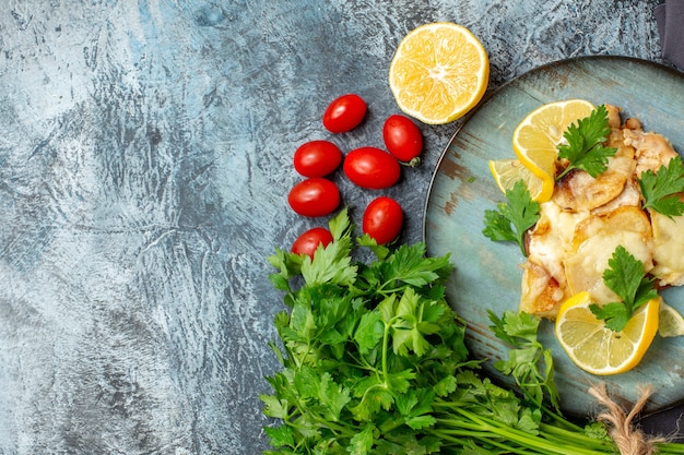 Vista superior de la mitad de pollo con queso en la placa manojo de perejil medio limón tomates cherry en el lugar de copia de mesa gris