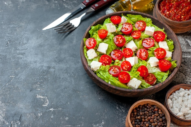 Vista superior de la mitad de la sabrosa ensalada de verduras con queso en rodajas, tomates y ensalada verde con condimentos sobre fondo oscuro, almuerzo, dieta saludable, comida, comida