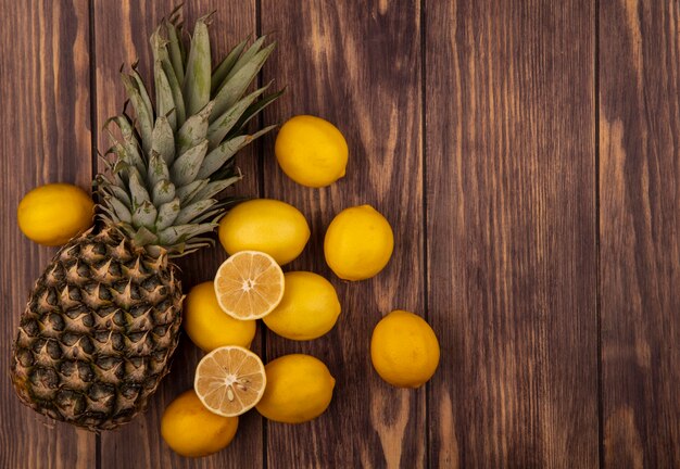 Vista superior de la mitad sana y limones enteros con piña aislado en una superficie de madera con espacio de copia