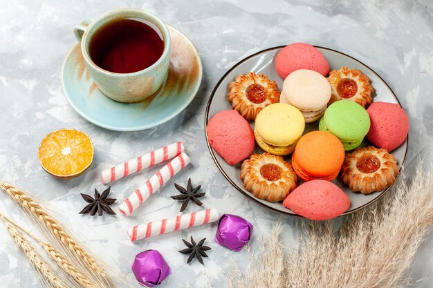 Vista superior de la mitad de una taza de té con galletas y macarons franceses en la superficie de color blanco claro caramelo dulce pastel de azúcar hornear galletas