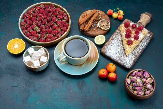 Vista superior de la mitad de un trozo de tarta horneada dulce con frambuesas y té en el escritorio oscuro pastel de azúcar baya pastel hornear galletas