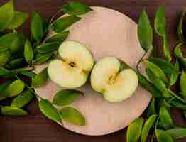 Foto gratuita vista superior de las mitades de una manzana verde en un soporte con ramas de hojas sobre una superficie marrón