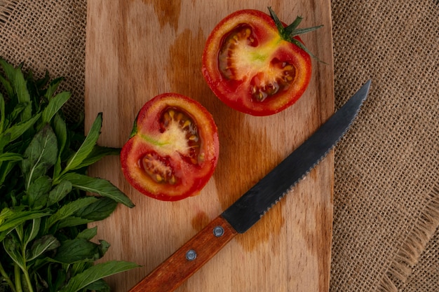 Vista superior de las mitades de tomate con un cuchillo sobre una tabla de cortar con un manojo de menta en una servilleta beige