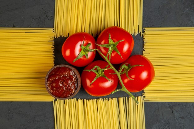 Vista superior montón de tomates con salsa de tomate y espagueti crudo en forma de decoración