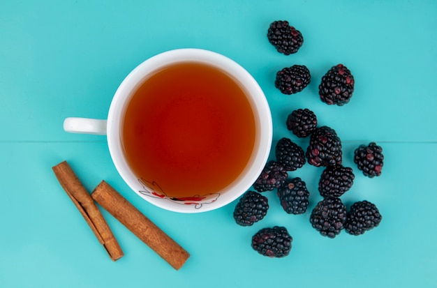 Foto gratuita vista superior de la mora con una taza de té y canela sobre una superficie turquesa