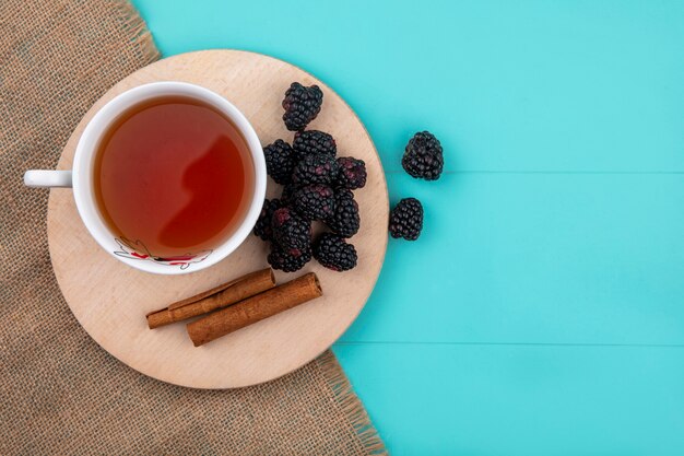 Vista superior de la mora con una taza de té y canela en un soporte sobre una superficie turquesa