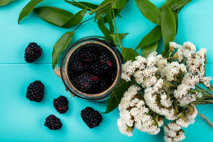 Foto gratuito vista superior de moras en un frasco con una rama de hojas y flores blancas en una superficie azul claro