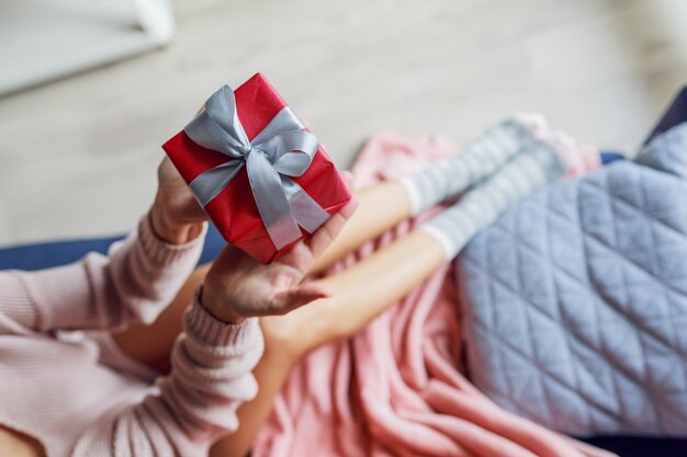 Vista superior de una mujer bonita con caja de regalo, sentada en el sofá de la casa. Foto suave. Concepto de vacaciones.