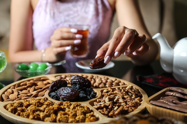 Vista superior mujer comiendo caqui seco con té y una mezcla de nueces y chocolate sobre la mesa