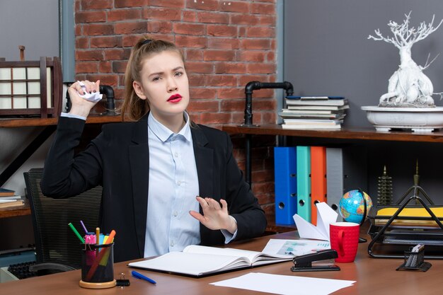 Vista superior de la mujer concentrada sentada en una mesa y sosteniendo papel envuelto en la oficina