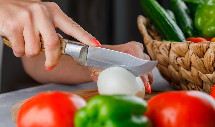 Foto gratuito vista superior, mujer, cortar la cebolla por la mitad en la tabla de cortar con cuchillo, pimiento verde, pepino, sal en la superficie gris