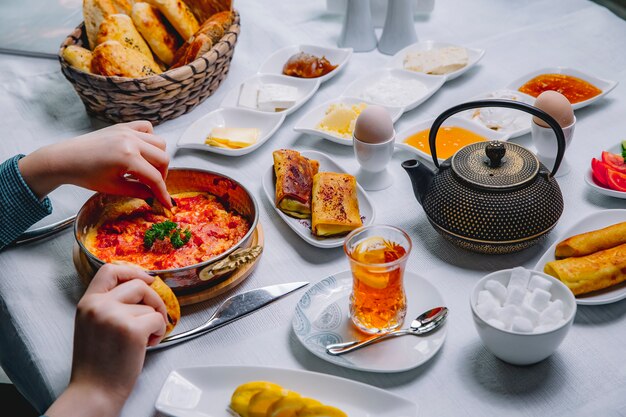 Vista superior una mujer desayuna huevos fritos con tomate en una sartén con panqueques y un vaso de té