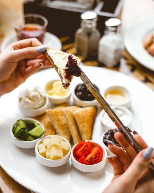 Vista superior una mujer desayuna tostadas fritas con mantequilla de miel, mermelada de crema agria y aceitunas en un plato