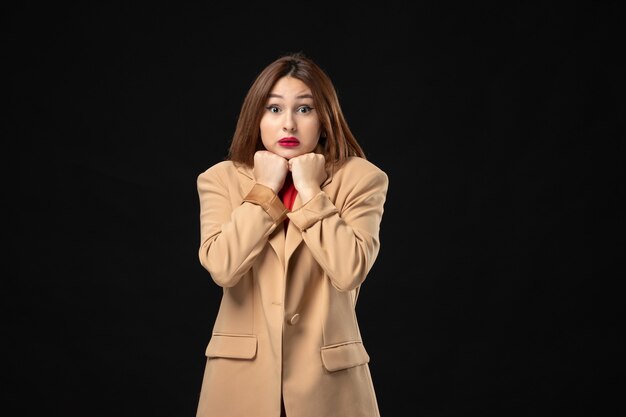 Vista superior de la mujer joven asustada en un traje marrón claro posando para la cámara en la oscuridad