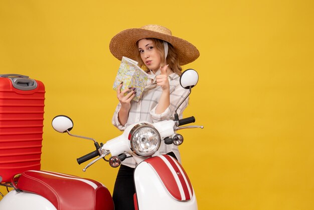 Vista superior de la mujer joven confiada con sombrero recogiendo su equipaje sentado en una motocicleta y sosteniendo el mapa