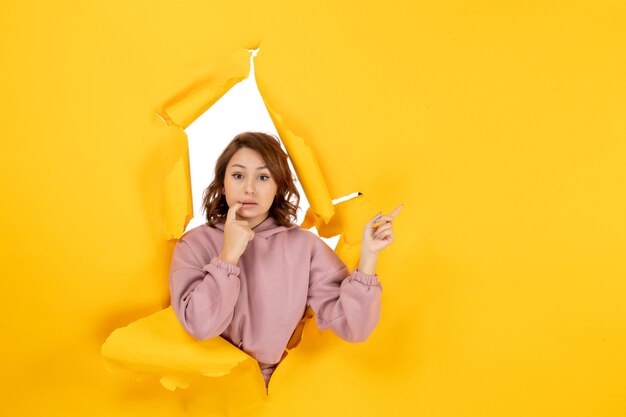 Vista superior de la mujer joven confundida señalando algo y espacio libre en amarillo rasgado