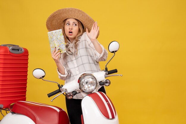 Vista superior de la mujer joven preguntándose con sombrero recogiendo su equipaje sentado en una motocicleta y sosteniendo el mapa