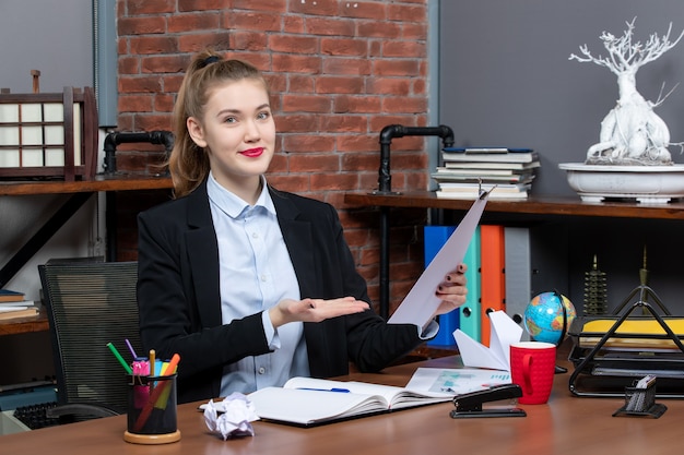 Foto gratuita vista superior de la mujer joven sentada en una mesa y mostrando el documento en la oficina