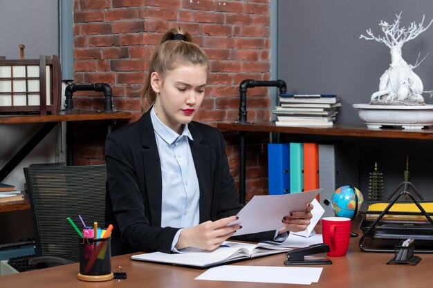 Vista superior de una mujer joven sentada en una mesa y sosteniendo un documento leyendo algo cuidadosamente en la oficina