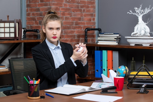 Vista superior de la mujer joven sentada en una mesa y sosteniendo papel envuelto en la oficina