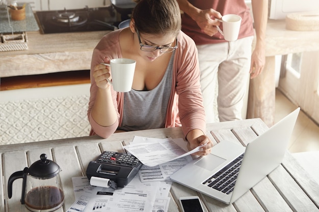 Vista superior de la mujer joven seria con gafas gestionando el presupuesto familiar