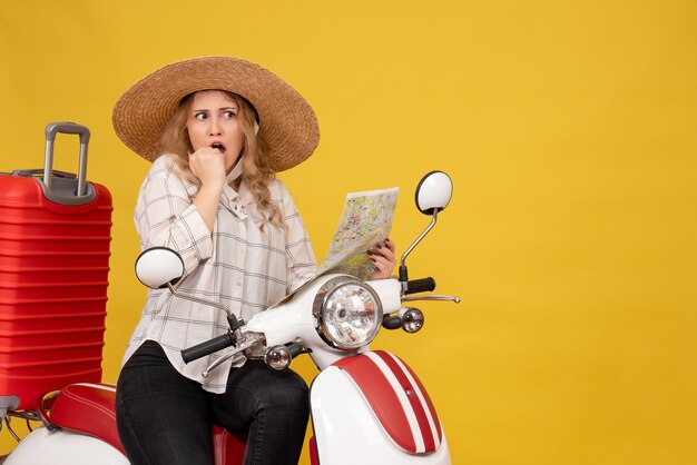 Vista superior de una mujer joven con sombrero y sentada en una motocicleta y sosteniendo el mapa sintiéndose sorprendido en amarillo