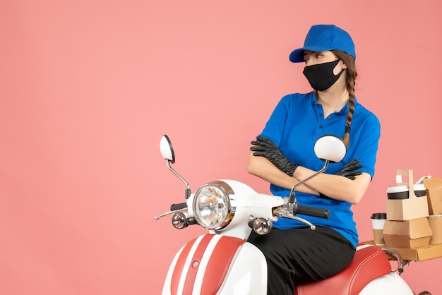 Vista superior de la mujer de mensajería reflexiva con máscara médica y guantes sentado en scooter entregando pedidos en melocotón pastel