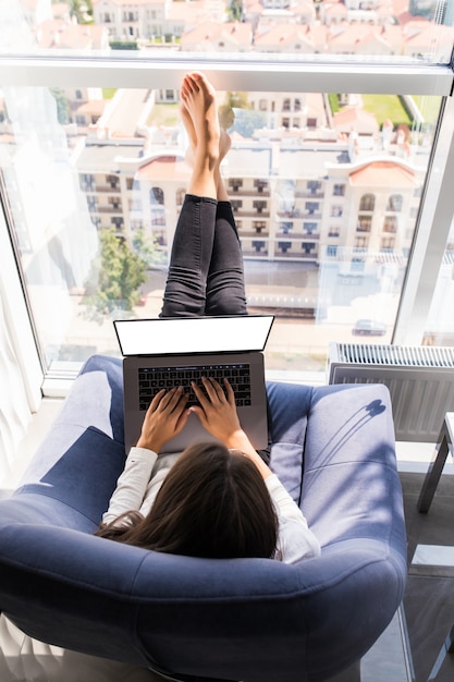 Vista superior de la mujer relajada que trabaja desde su casa con la computadora en una mecedora