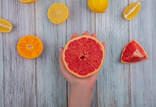 Vista superior mujer sostenga en la mano medio pomelo con naranja y limón sobre fondo gris