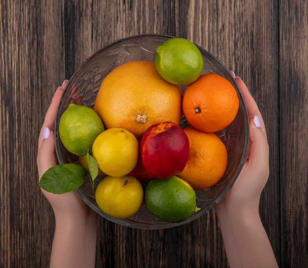 Foto gratuita vista superior mujer sosteniendo un jarrón con mezcla de frutas pomelo naranjas limas ciruela y melocotón sobre fondo de madera