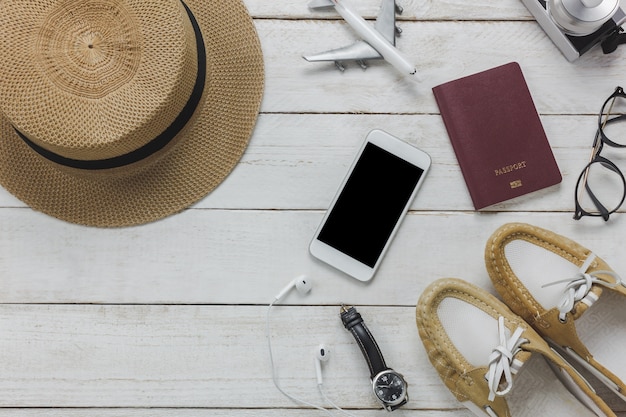 Vista superior mujeres accesorios para viajar concept.White teléfono móvil, avión, sombrero, pasaporte, reloj, anteojos en mesa de madera.