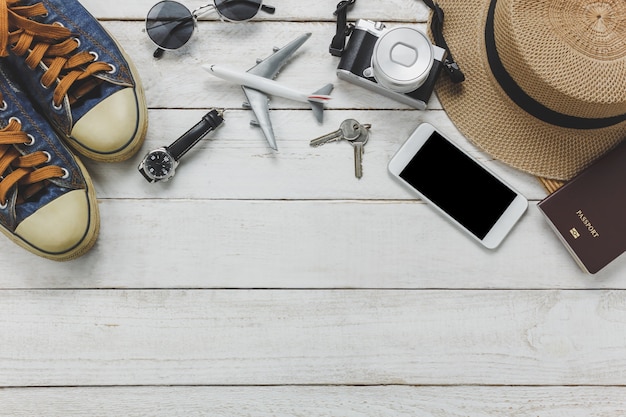 Vista superior de las mujeres accesorios para viajar concept.White teléfono móvil, avión, sombrero, pasaporte, reloj, gafas de sol sobre la mesa de madera.