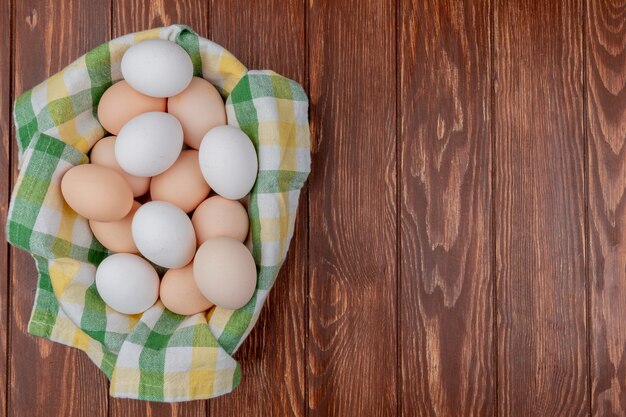 Vista superior de múltiples huevos de gallina fresca sobre un mantel marcado sobre un fondo de madera con espacio de copia