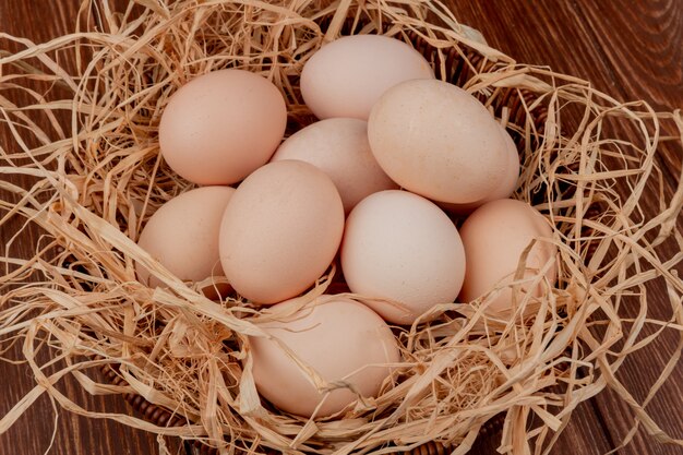 Vista superior de múltiples huevos de gallina en el nido sobre fondo de madera