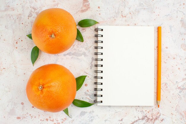 Vista superior de naranjas frescas cuaderno naranja lápiz sobre brillante superficie aislada