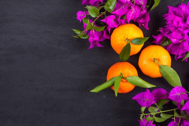 Vista superior de naranjas frescas con flores de color púrpura con espacio de copia en superficie oscura