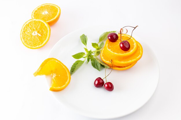 Vista superior de naranjas frescas en rodajas dentro de un plato blanco junto con cerezas rojas sobre el fondo blanco jugo de frutas exóticas
