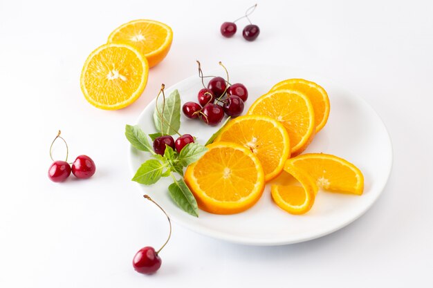 Vista superior de naranjas frescas en rodajas dentro de un plato blanco junto con cerezas rojas sobre el fondo claro jugo de color de frutas exóticas