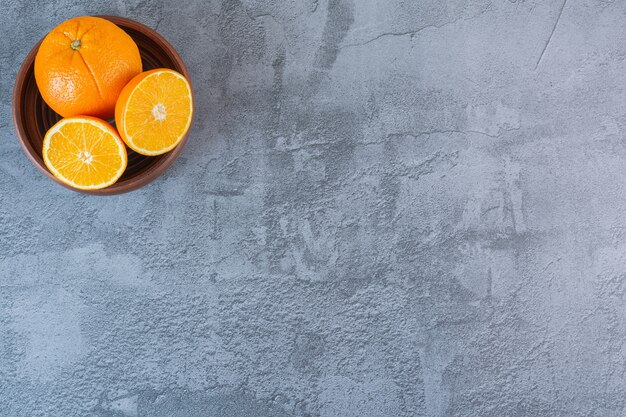 Vista superior de naranjas jugosas frescas en un tazón de madera sobre gris.